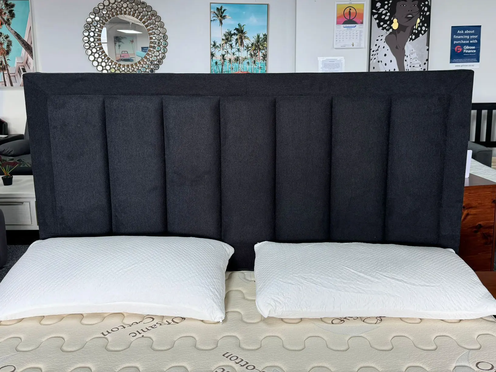 A wide charcoal panelled headboard behind a mattress in the showroom.
