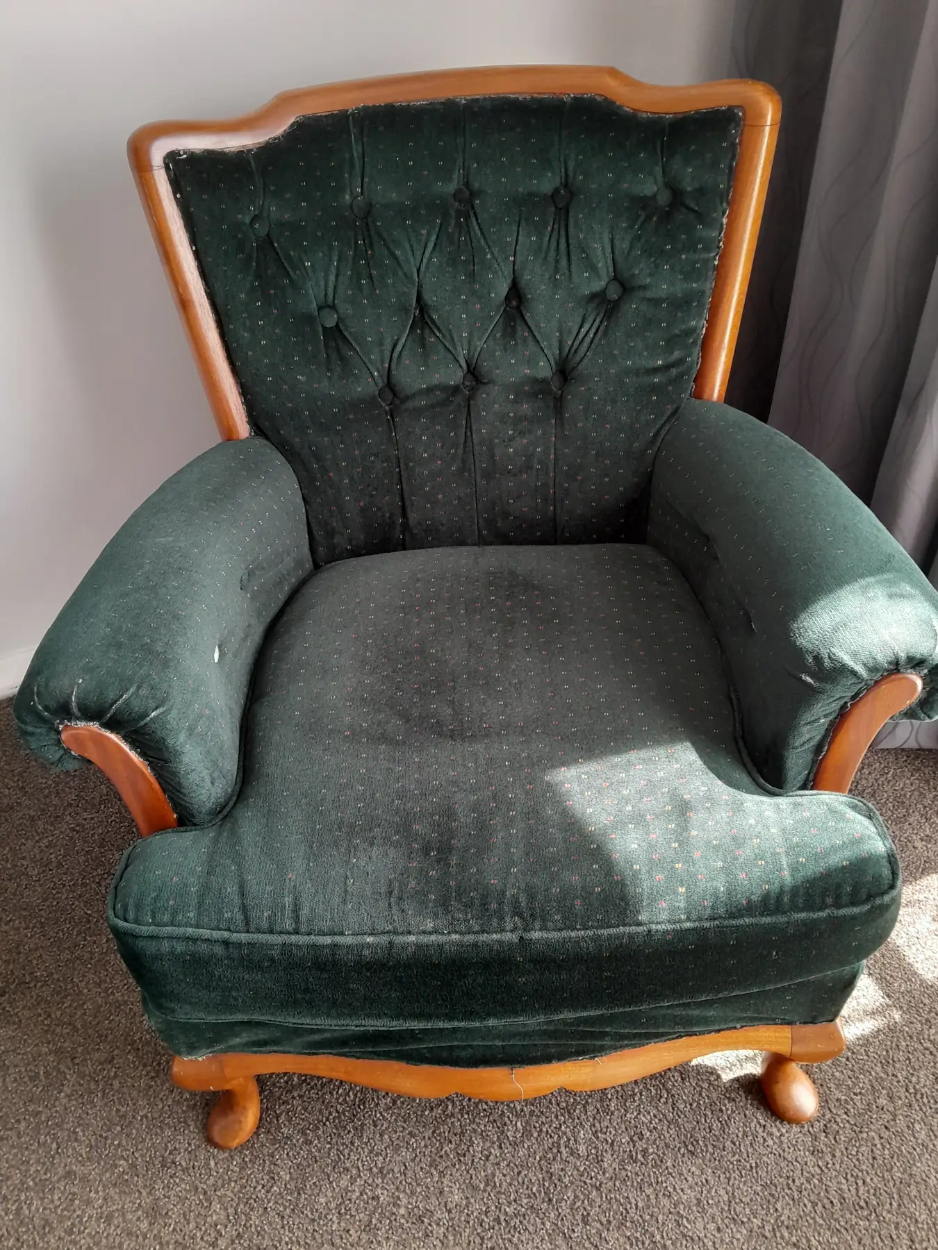 A deep green velvet armchair with a carved timber frame and buttoned back, before work.