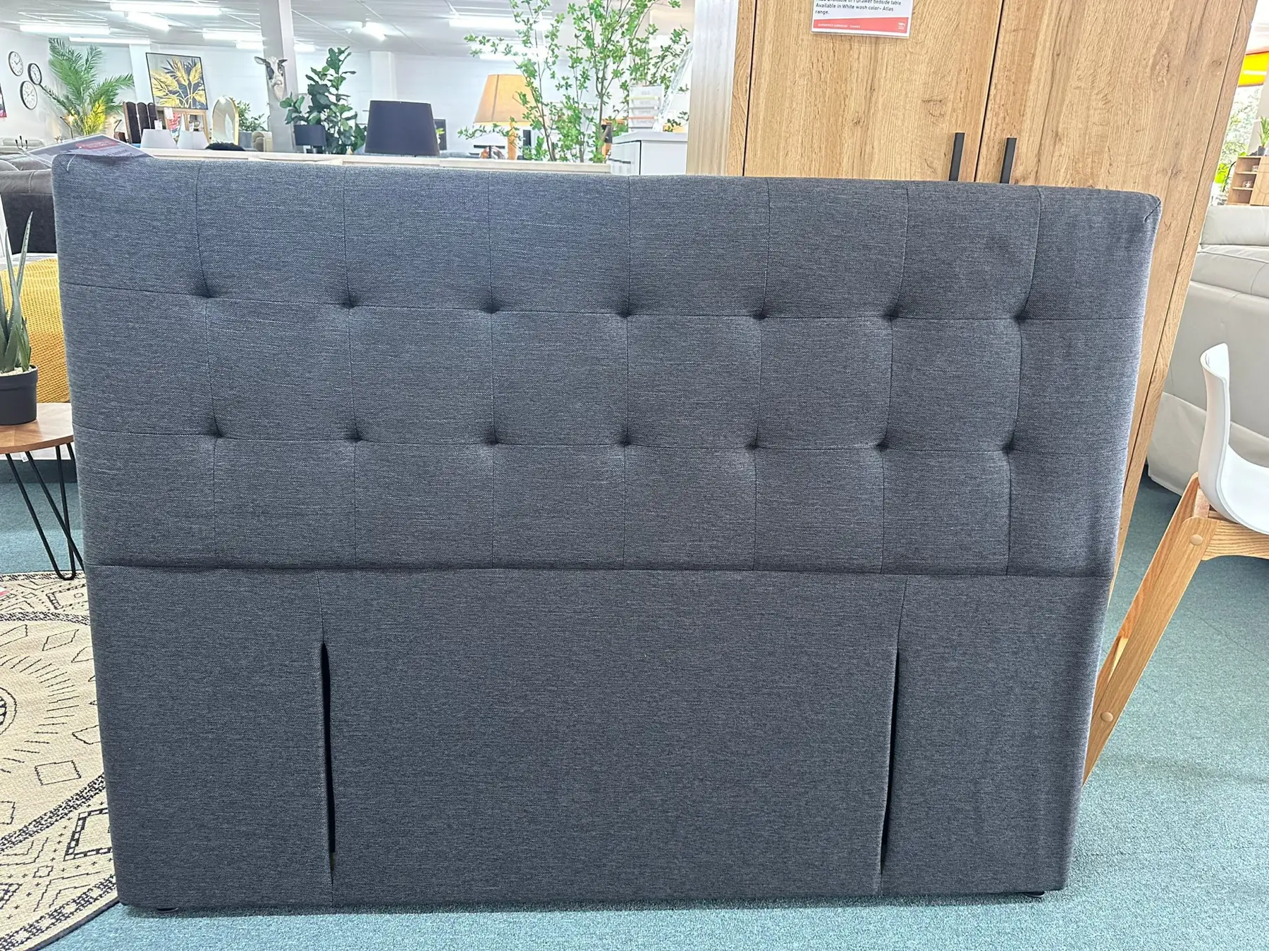 A grey buttoned headboard with a shaped top, on the showroom floor.