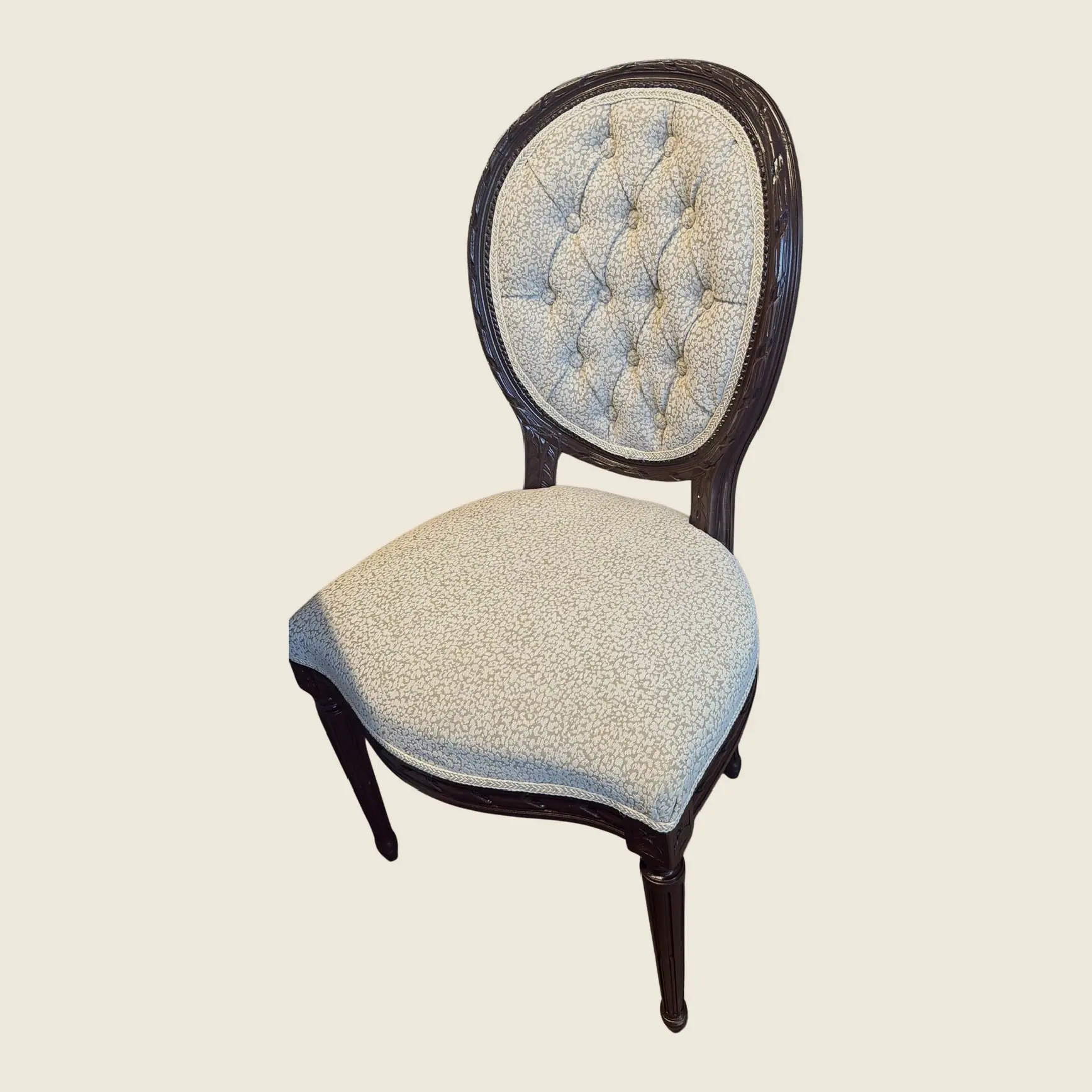 A carved dining chair with a button-tufted oval back, front three-quarter view