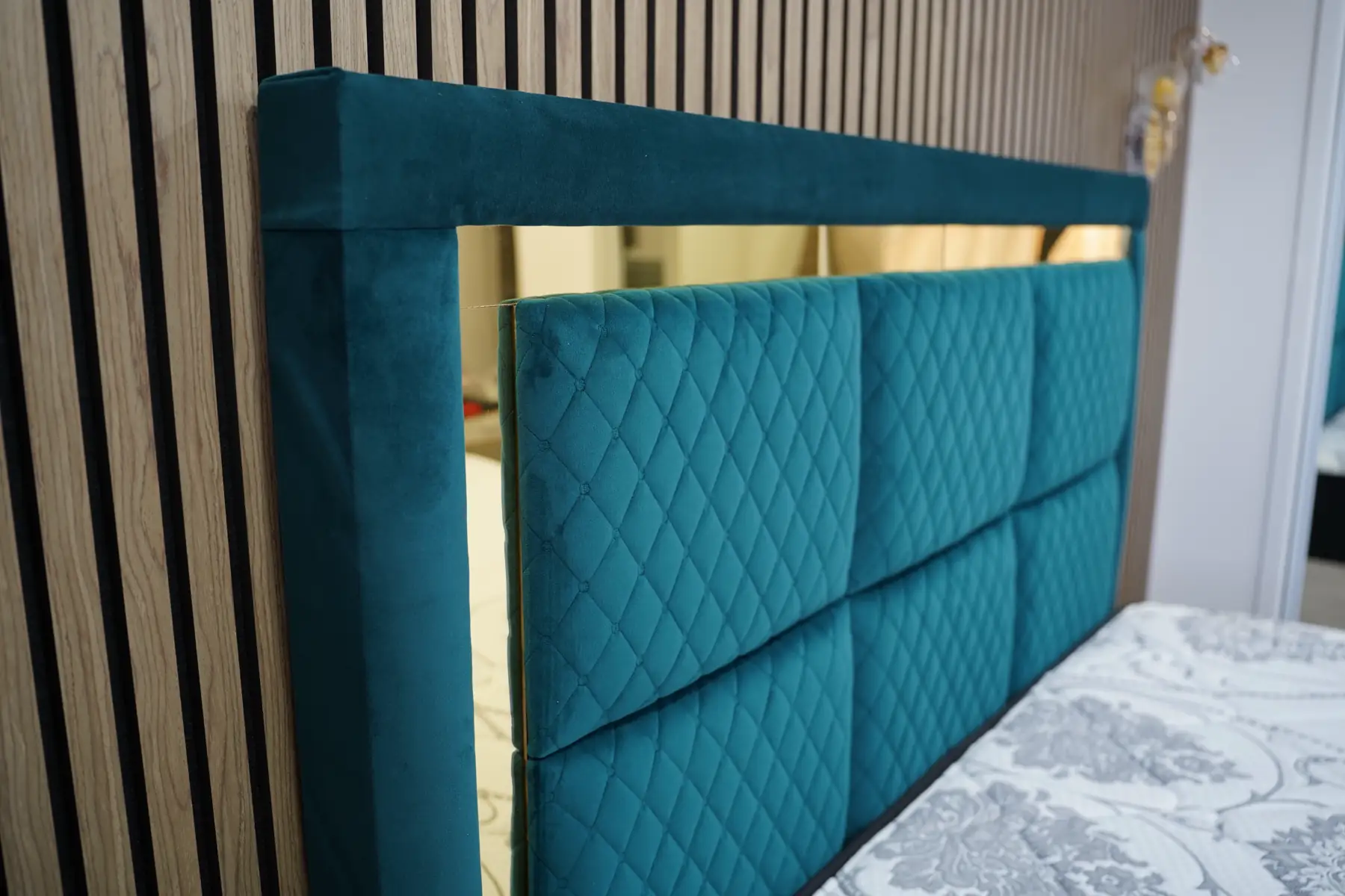 The teal velvet and gold headboard from the side, showing the depth of the board and the mitred gold frame.