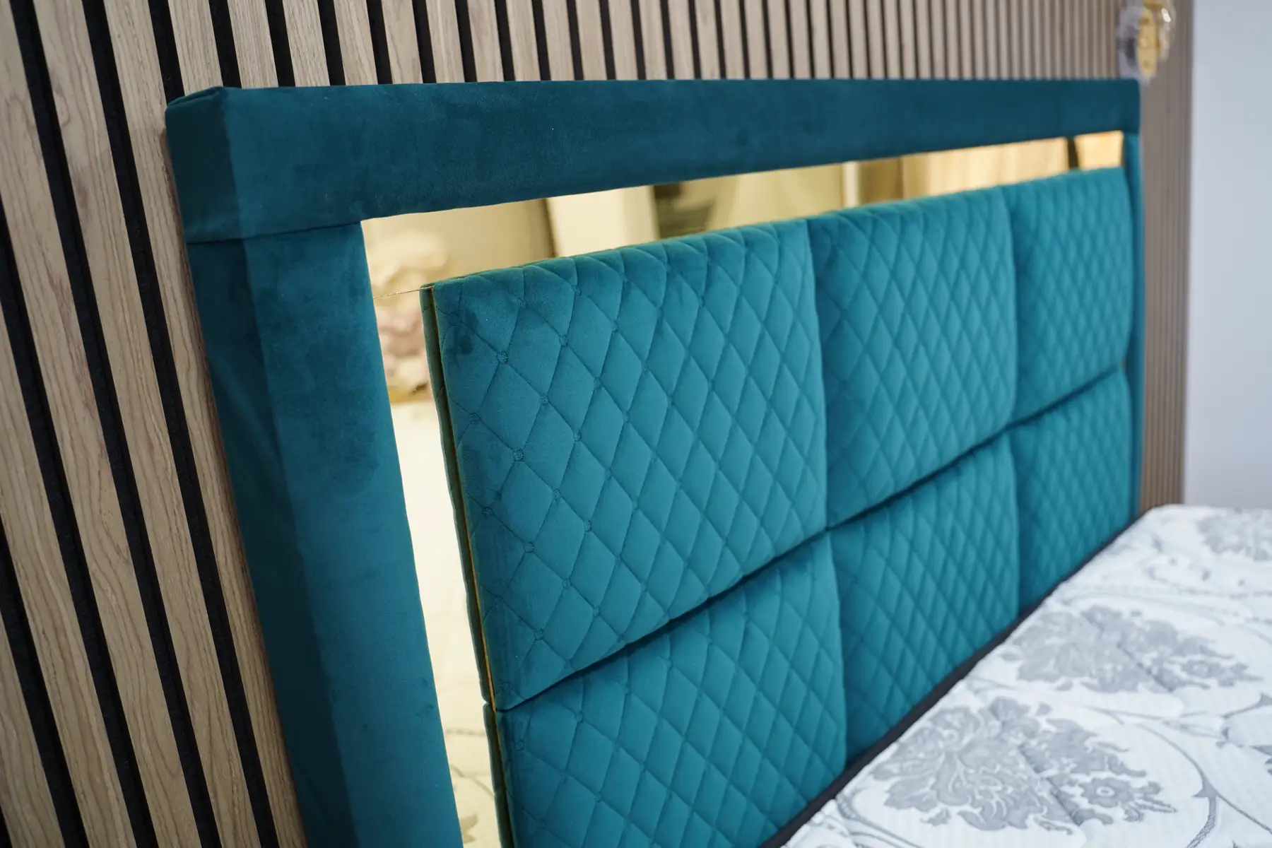 Close on the diamond quilting of the teal velvet headboard where it meets the gold frame.